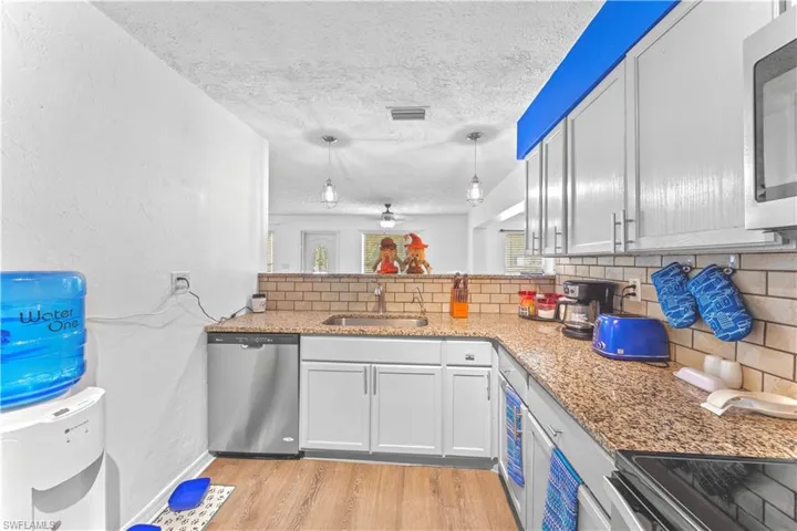 Kitchen with appliances with stainless steel finishes, white cabinetry, hanging light fixtures, and light hardwood / wood-style floors