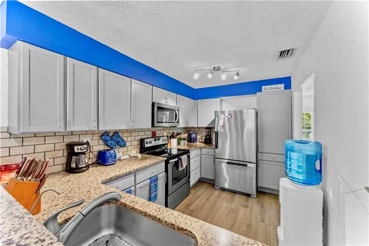 Kitchen featuring decorative backsplash, sink, white cabinets, appliances with stainless steel finishes, and a textured ceiling