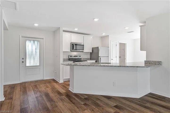Kitchen with dark hardwood / wood-style flooring, appliances with stainless steel finishes, white cabinets, kitchen peninsula, and light stone counters