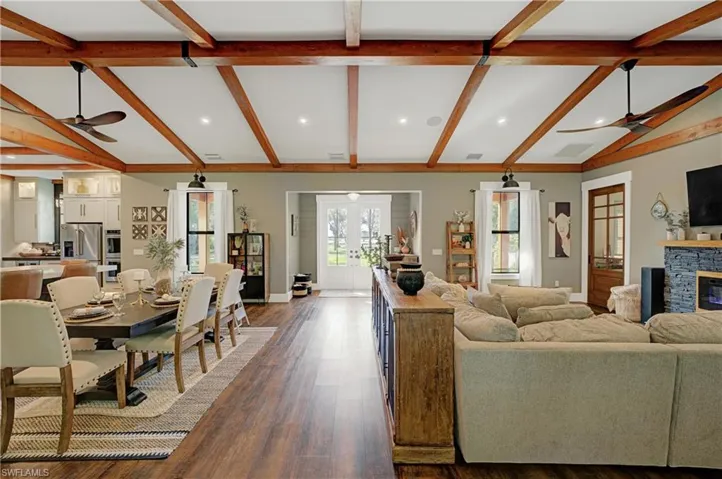 Living room with french doors, ceiling fan, beam ceiling, dark hardwood / wood-style floors, and a stone fireplace