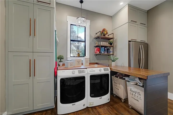 Washroom with cabinets, washer and dryer, dark wood-type flooring, and an inviting chandelier