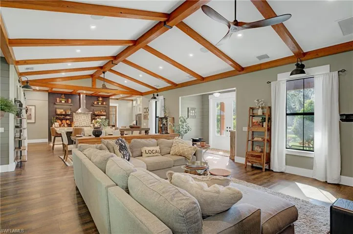 Living room featuring vaulted ceiling with beams, ceiling fan, and wood-type flooring