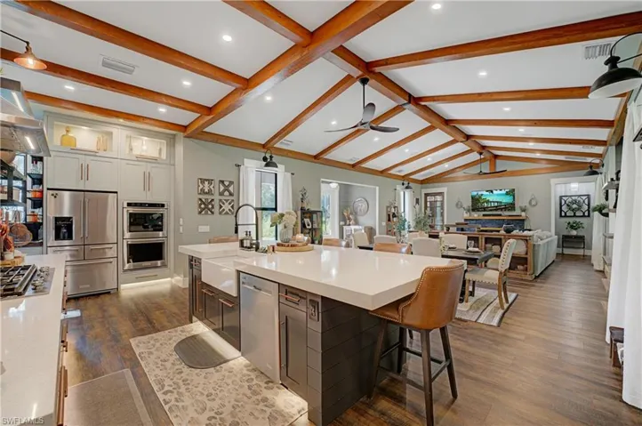 Kitchen with appliances with stainless steel finishes, ceiling fan, dark wood-type flooring, a spacious island, and vaulted ceiling with beams