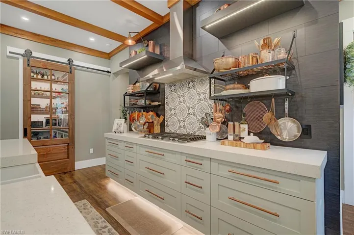 Kitchen featuring island range hood, stainless steel gas cooktop, dark wood-type flooring, beam ceiling, and a barn door