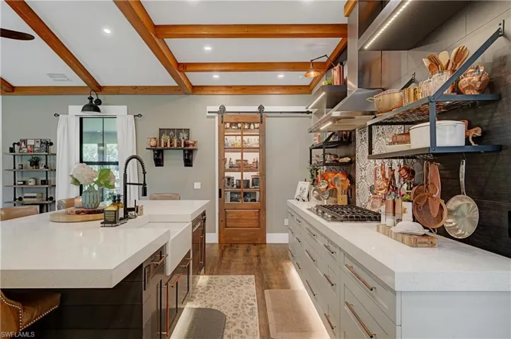 Kitchen featuring stainless steel gas cooktop, a spacious island, beam ceiling, a barn door, and white cabinetry