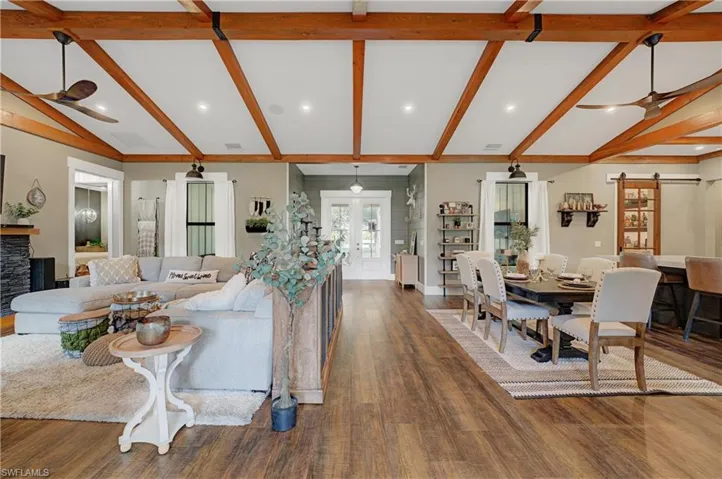 Living room with lofted ceiling with beams, a barn door, dark hardwood / wood-style floors, and ceiling fan