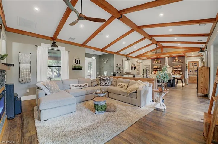 Living room with ceiling fan, dark hardwood / wood-style flooring, and lofted ceiling with beams