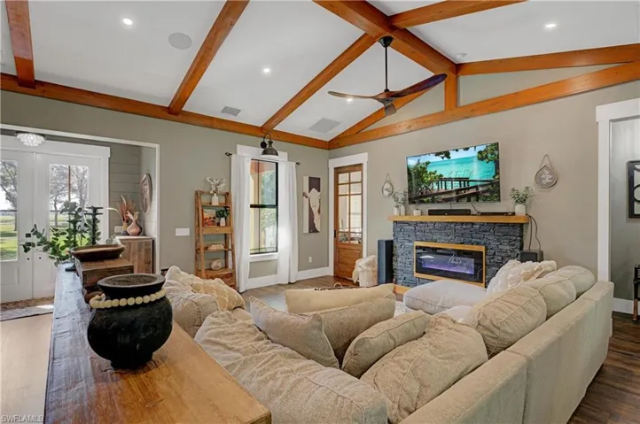 Living room featuring lofted ceiling with beams, a stone fireplace, a wealth of natural light, and dark wood-type flooring