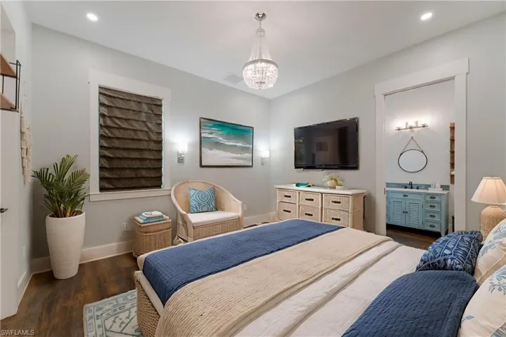 Bedroom featuring ensuite bathroom, dark hardwood / wood-style floors, and a notable chandelier - virtually staged