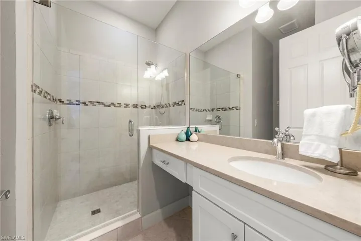 Guest bathroom featuring a vanity with a neutral solid-surface countertop, an integrated oval sink, a wall-to-wall mirror, and a walk-in shower with a glass enclosure and decorative tile inlay