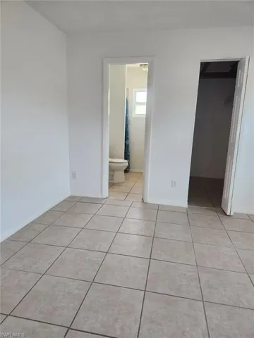 Unfurnished bedroom featuring a walk in closet, light tile patterned flooring, and ensuite bath