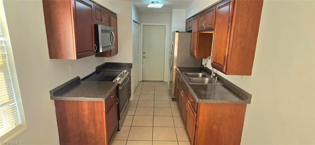 Kitchen featuring dark countertops, stainless steel appliances, light tile patterned floors, and reddish brown cabinets
