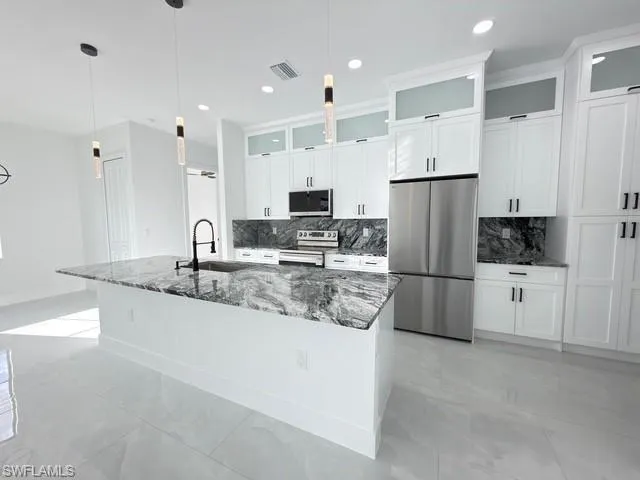 Kitchen with stainless steel appliances, glass fronted cabinets, dark stone counters, white cabinetry, and a large island with sink