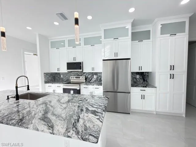 Kitchen with glass fronted cabinets, stainless steel appliances, decorative backsplash, and pendant lighting