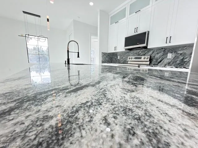 Kitchen featuring glass fronted cabinets, white cabinetry, light stone countertops, stainless steel electric stove, and decorative light fixtures