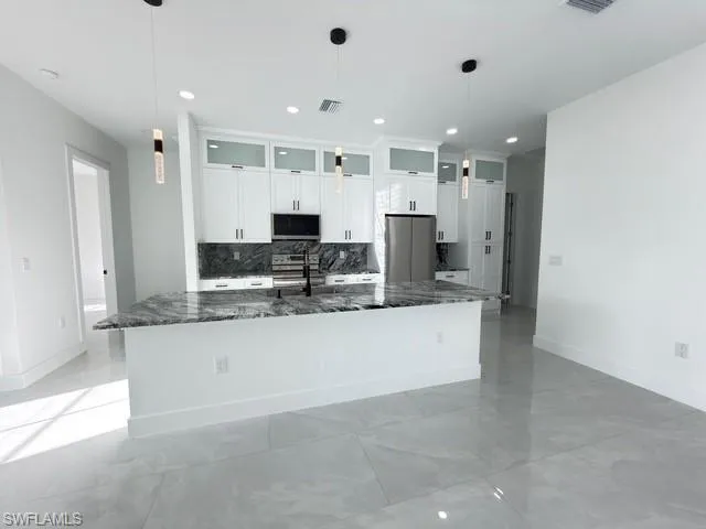 Kitchen with white cabinets, glass fronted cabinets, a large island with sink, and stainless steel appliances