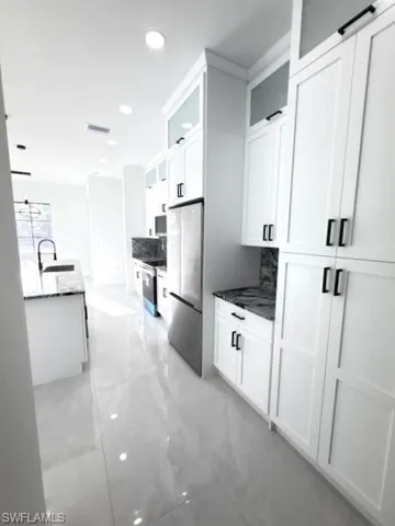 Kitchen featuring glass fronted cabinets, white cabinets, stainless steel appliances, dark stone counters, and pendant lighting