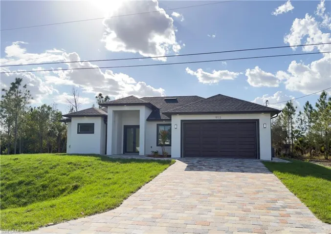 Prairie-style home featuring a front yard, stucco siding, a garage, decorative driveway, and roof with shingles
