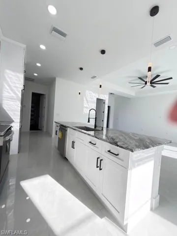 Kitchen featuring decorative light fixtures, white cabinetry, dark stone counters, stainless steel appliances, and an island with sink