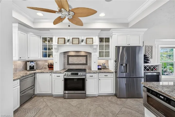 Kitchen with stainless steel appliances, glass fronted cabinets, ceiling fan, white cabinetry, and recessed lighting