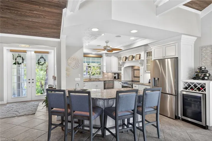 Kitchen featuring a kitchen breakfast bar, light stone counters, stainless steel appliances, wine cooler, and glass fronted cabinets