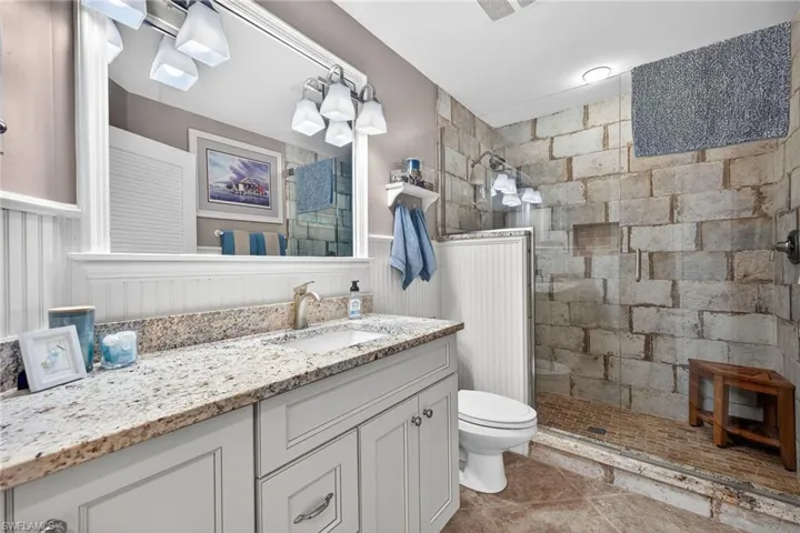Full bath featuring vanity, a walk in shower, wainscoting, and light tile patterned flooring