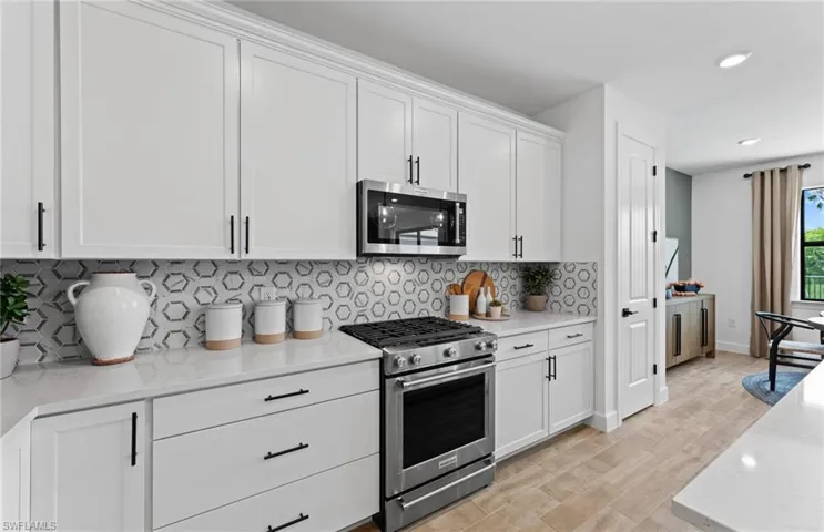 Kitchen featuring stainless steel appliances, white cabinetry, light stone countertops, light wood-style flooring, and backsplash