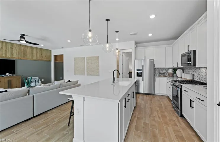 Kitchen with open floor plan, stainless steel appliances, white cabinets, a breakfast bar area, and an island with sink