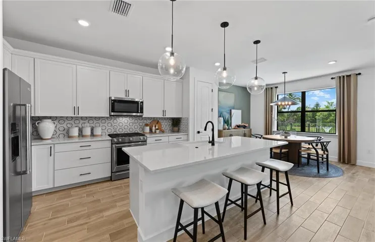 Kitchen with decorative backsplash, white cabinets, stainless steel appliances, a breakfast bar, and wood tiled floors