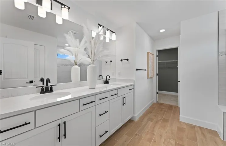 Bathroom featuring double vanity, wood finish floors, a walk in closet, and recessed lighting
