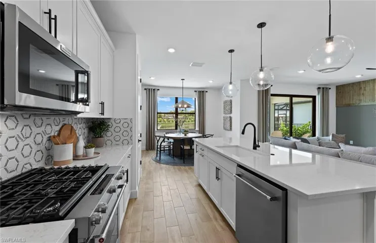Kitchen with white cabinetry, stainless steel appliances, light stone counters, wood finish floors, and open floor plan