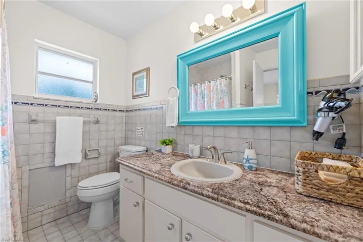 Bathroom featuring vanity, tile walls, wainscoting, a shower with shower curtain, and light tile patterned flooring