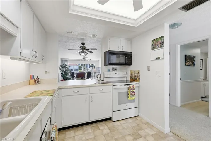 Kitchen featuring white electric stove, a ceiling fan, white cabinetry, light countertops, and black microwave