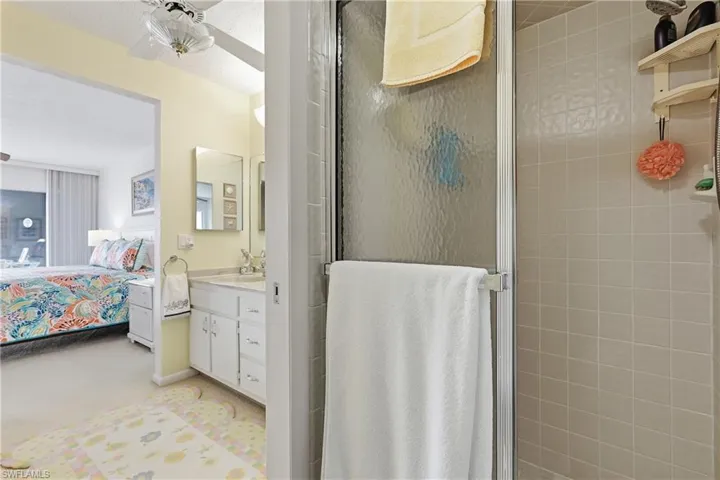 Ensuite bathroom with a stall shower, vanity, light colored carpet, and a ceiling fan