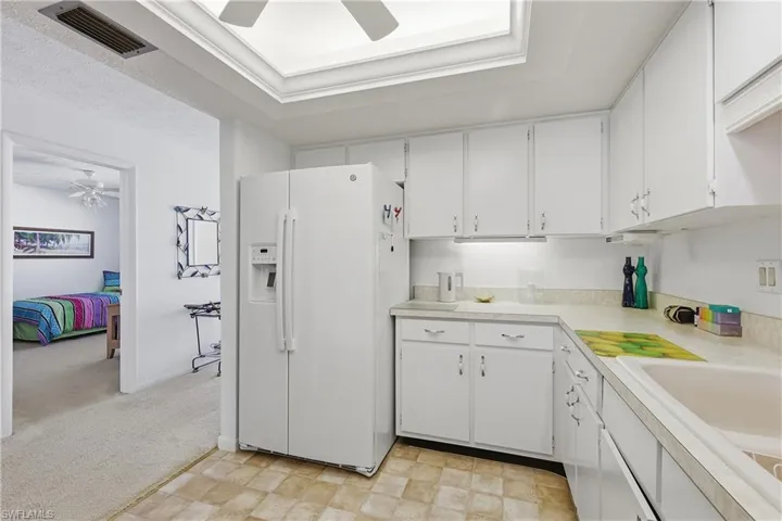 Kitchen featuring ceiling fan, white refrigerator with ice dispenser, white cabinets, light countertops, and a raised ceiling