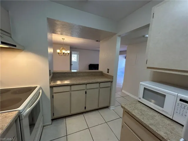 Kitchen with white appliances, hanging lights, light tile patterned flooring, and light stone counters