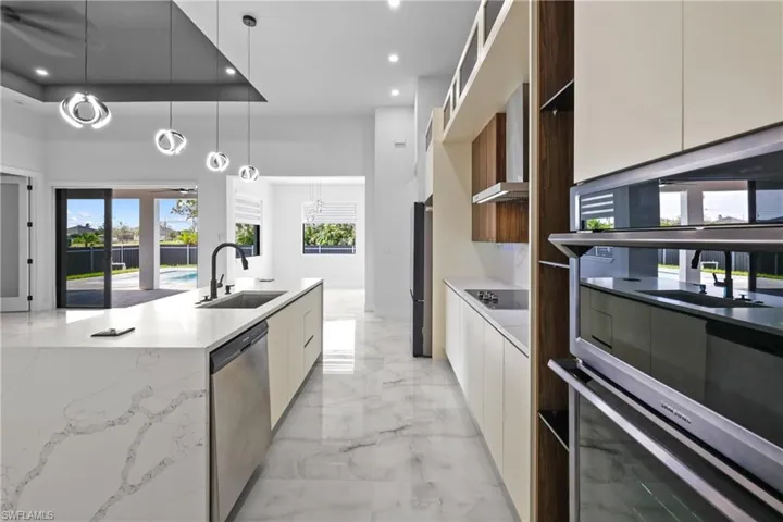 Kitchen featuring appliances with stainless steel finishes, sink, a tray ceiling, hanging light fixtures, and light stone counters