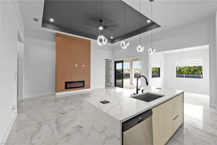 Kitchen with light stone counters, a kitchen island with sink, a tray ceiling, dishwasher, and sink
