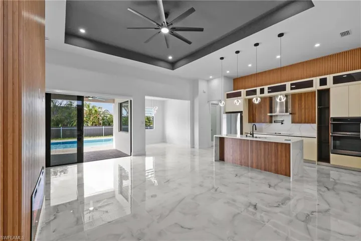Kitchen featuring appliances with stainless steel finishes, hanging light fixtures, a tray ceiling, and wall chimney range hood