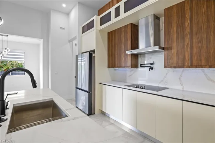 Kitchen with sink, white cabinets, wall chimney range hood, and stainless steel refrigerator