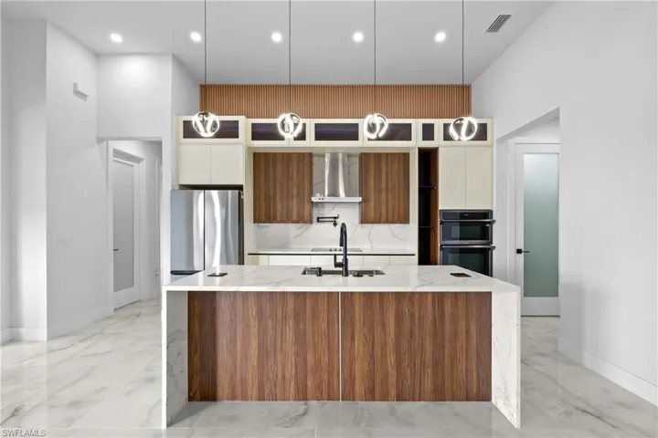 Kitchen with double oven, light stone countertops, pendant lighting, white cabinetry, and stainless steel refrigerator