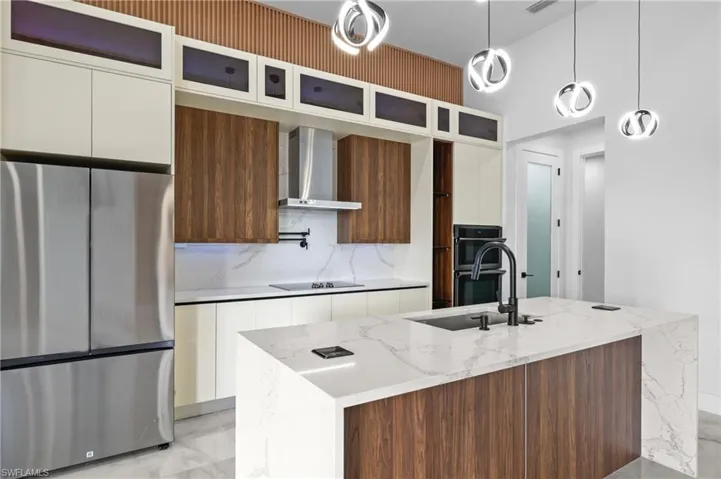 Kitchen featuring wall chimney exhaust hood, an island with sink, hanging light fixtures, sink, and black appliances