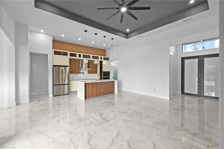 Kitchen with wall chimney range hood, a kitchen island, a tray ceiling, hanging light fixtures, and stainless steel appliances