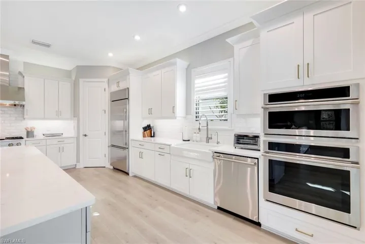 Kitchen with stainless steel appliances, white cabinetry, crown molding, light stone countertops, and wall chimney exhaust hood