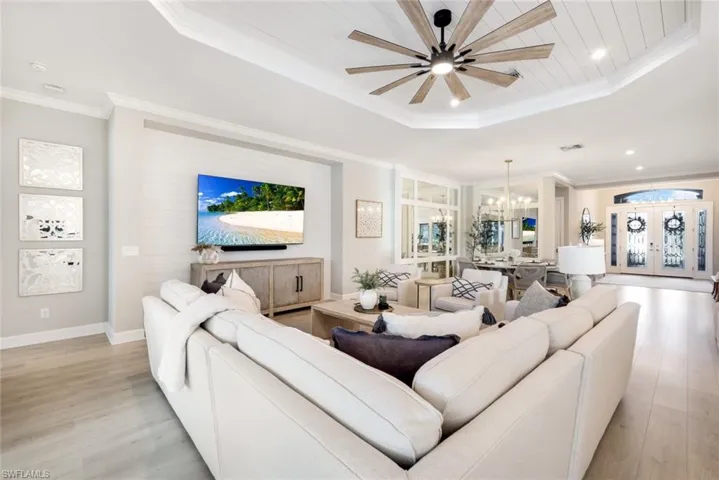 Living room featuring a tray ceiling, french doors, ornamental molding, light wood-style flooring, and a chandelier