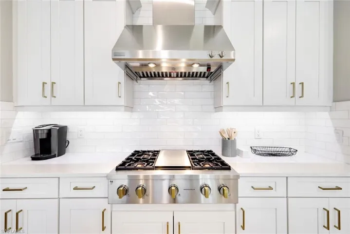 Kitchen with wall chimney range hood, stainless steel gas cooktop, white cabinets, and light stone countertops