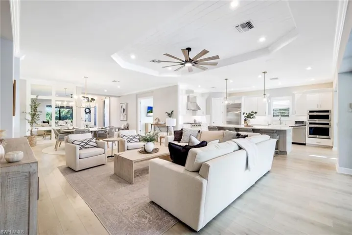 Living area featuring light wood-style flooring, ornamental molding, a chandelier, a raised ceiling, and a ceiling fan