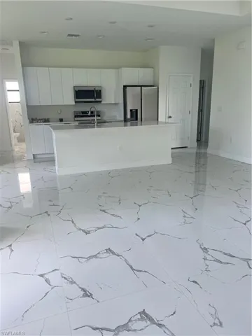 Kitchen with white cabinetry, stove, an island with sink, fridge, and light tile floors