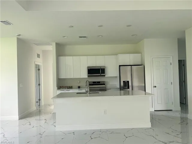 Kitchen featuring a center island with sink, appliances with stainless steel finishes, and light tile floors