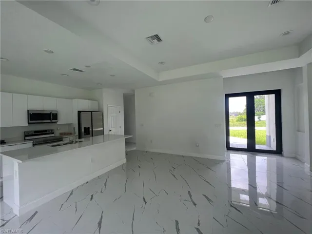 Kitchen featuring white cabinets, light tile flooring, a center island with sink, and stainless steel appliances